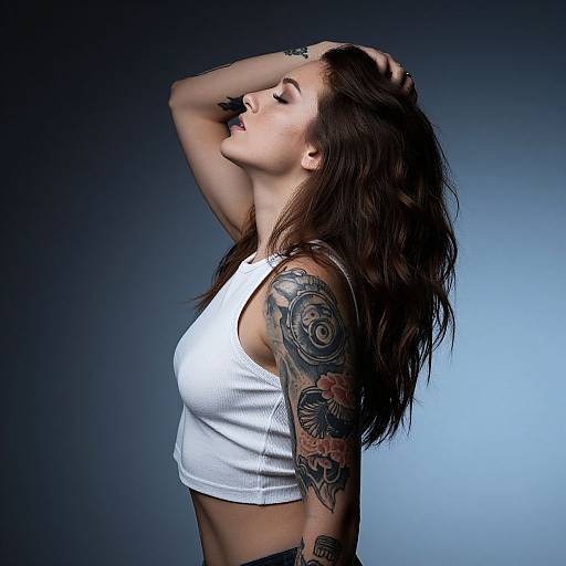 Tattooed woman with long brown hair, white crop top, eyes closed, hand on head, against blue gradient background, showcasing arm tattoos.