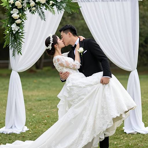 Photograph of a Chinese couple kissing at an outdoor wedding, the bride in a white lace dress and the groom in a black suit, standing under a