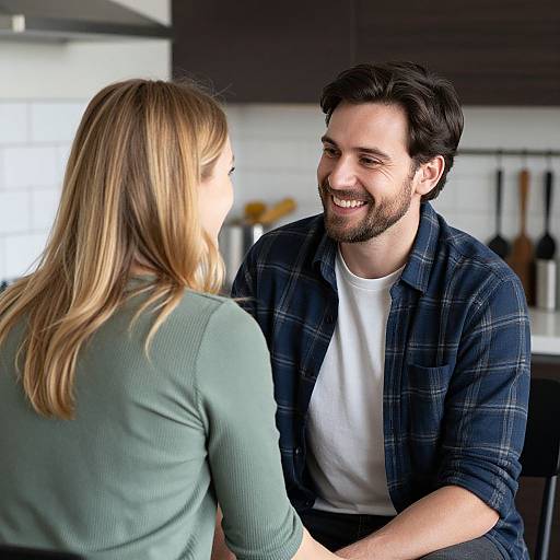 Photograph of a smiling, bearded man with dark hair in a blue plaid shirt, sitting across from a blonde woman in a green top,