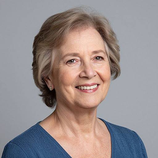 Photograph of a smiling middle-aged woman with short, light brown hair, wearing a blue V-neck sweater, against a plain gray background.