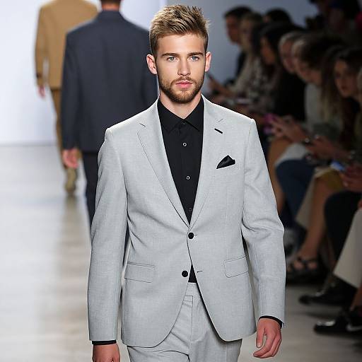 Photograph of a handsome, bearded model with short brown hair, wearing a light gray suit, black shirt, and pocket square, walking down a