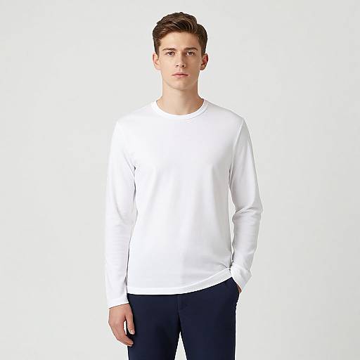 Photograph of a young man with short brown hair, wearing a plain white long-sleeve shirt and black pants, standing against a plain white background