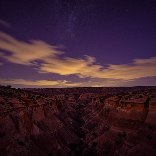 Photograph of a dramatic desert canyon at twilight, featuring deep red and orange rock formations, a darkening sky with vibrant yellow and purple clouds, and