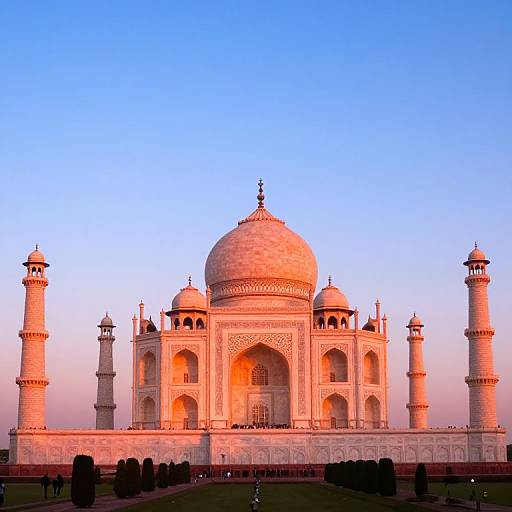 Photograph of the Taj Mahal at sunset, showcasing its white marble domes and minarets bathed in warm, pinkish light against a