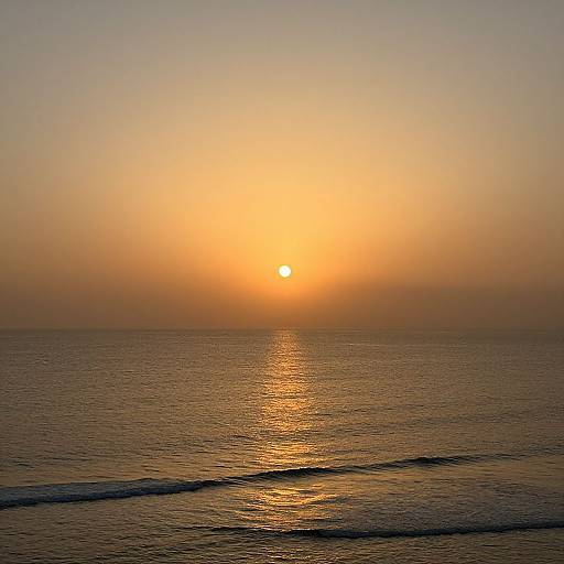 Photograph of a serene sunset over a calm ocean, with the sun glowing orange and casting a golden reflection on the water's surface.