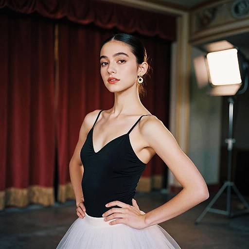 Photograph of a slender, fair-skinned ballerina with black top, white tutu, and dark hair in an elegant, dimly lit