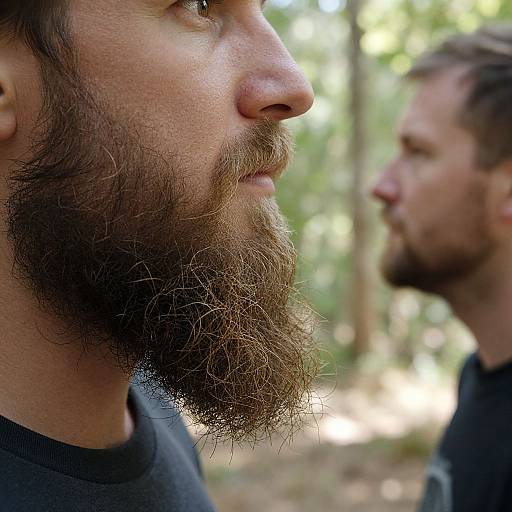 Close-up photograph of two bearded men in profile, one with a thick brown beard and the other with a trimmed beard, outdoors with a blurred forest