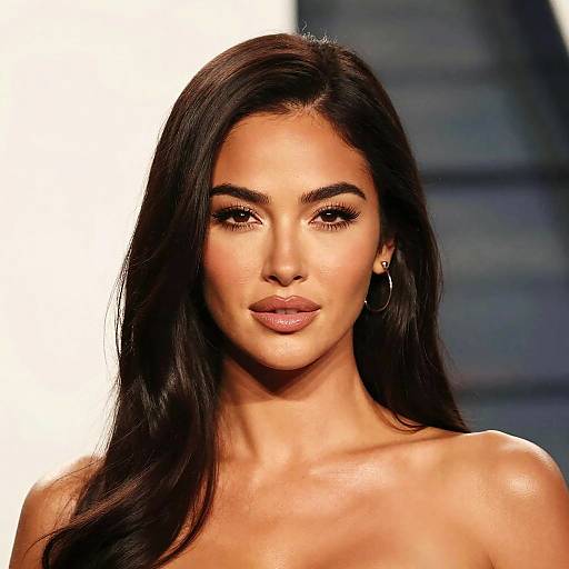 Photograph of Kim Kardashian with long, straight, dark brown hair, wearing hoop earrings, and a strapless top, against a blurred white and blue