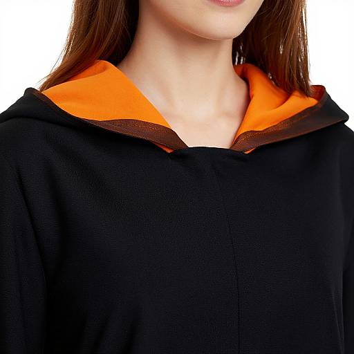 Photograph of a woman's neck and upper chest, wearing a black hoodie with a vivid orange hood lining, white background.
