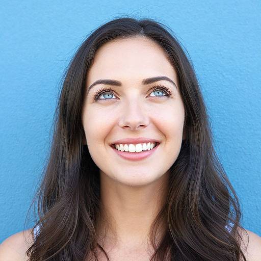 Photograph of a smiling young woman with long dark brown hair, blue eyes, and fair skin, set against a bright blue background. She looks upward