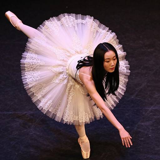 Photograph of an Asian ballerina with long black hair, wearing a white lace tutu and pink pointe shoes, gracefully extending her arm and