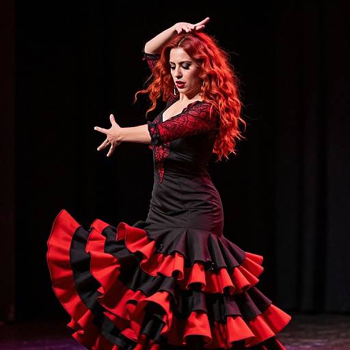 Photograph of a red-haired woman in a black dress with red ruffles, performing a flamenco dance on a dark stage.