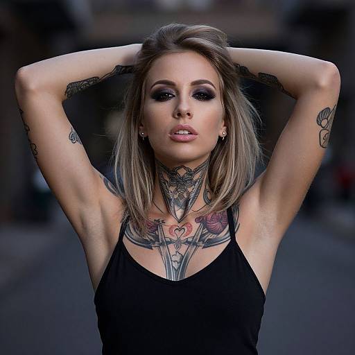 Photograph of a tattooed, blonde woman with hands behind head, black tank top, dark makeup, urban background, detailed chest and neck tattoos.