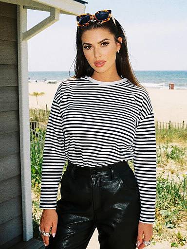 Photograph of a woman with long dark hair, wearing a black-and-white striped long-sleeve shirt, black leather pants, and sunglasses on head