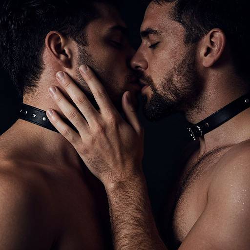 Photograph of two bearded, shirtless men with black leather collars, eyes closed, noses touching, one hand gently touching the other's cheek
