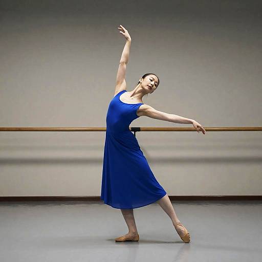 Photograph of a slender, light-skinned female ballet dancer in a blue sleeveless dress, balancing on pointe, arms gracefully extended, in a