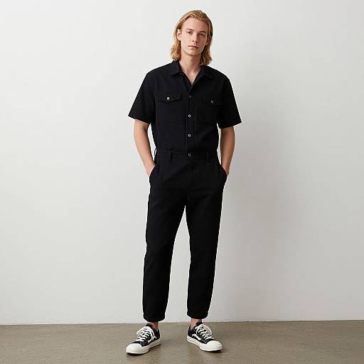 Photograph of a blonde, fair-skinned man with medium build, wearing a black short-sleeve button-up shirt and black pants, hands in