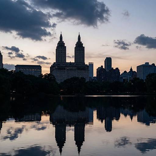 Photograph of a city skyline at dusk, featuring twin-towered buildings reflected in a calm river, with a cloudy, colorful sky.