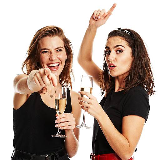 Photograph of two women with shoulder-length brown hair, wearing black tops, raising champagne glasses, and pointing with expressive, joyful faces against a white background