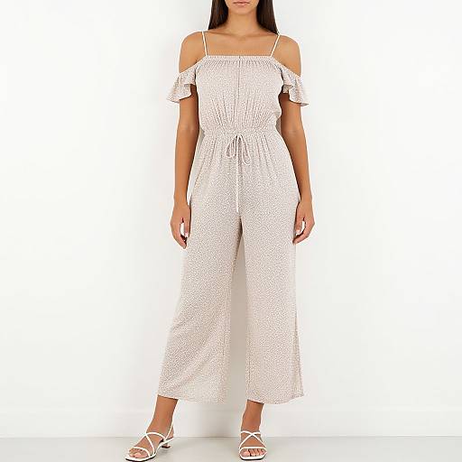 Photograph of a woman in a white, off-shoulder, high-waisted romper with small polka dots, standing against a plain