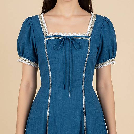 Photograph of a woman in a blue, short-sleeved, lace-trimmed, square-neck dress with a bow tie at the chest.