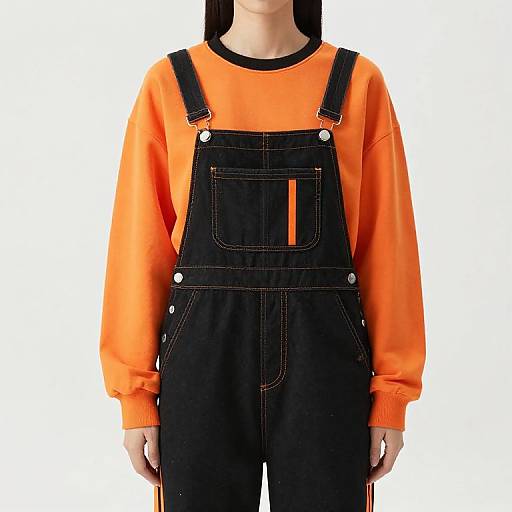 Photograph of a person wearing an orange long-sleeve shirt with black overalls, showing a front view against a plain white background.