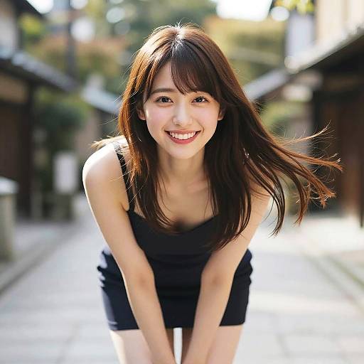 Photograph of smiling Asian woman with long brown hair, wearing a black strapless dress, leaning forward in a sunlit, narrow Japanese alley.