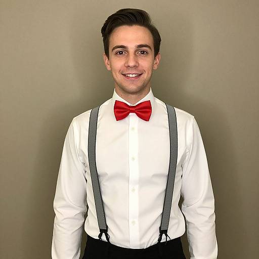 Photograph of a smiling young man with short dark hair, wearing a white shirt, red bow tie, black suspenders, and black pants, against