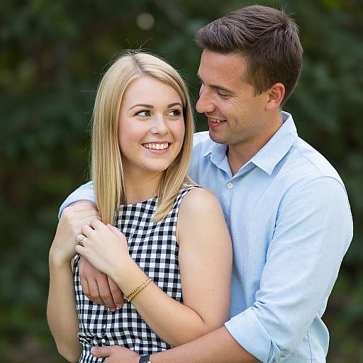 Photograph of a smiling blonde woman in a black-and-white checkered dress, being hugged from behind by a smiling brown-haired man in a white shirt