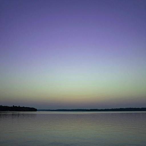 Photograph of a serene lake at dusk, with a gradient sky from blue to yellow, and a distant, dark shoreline.