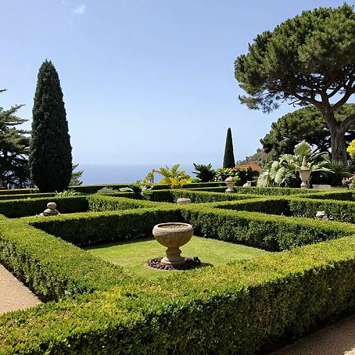 Photograph of a sunlit formal garden with green hedges, stone urns, tall cypress trees, and a clear blue sky backdrop.