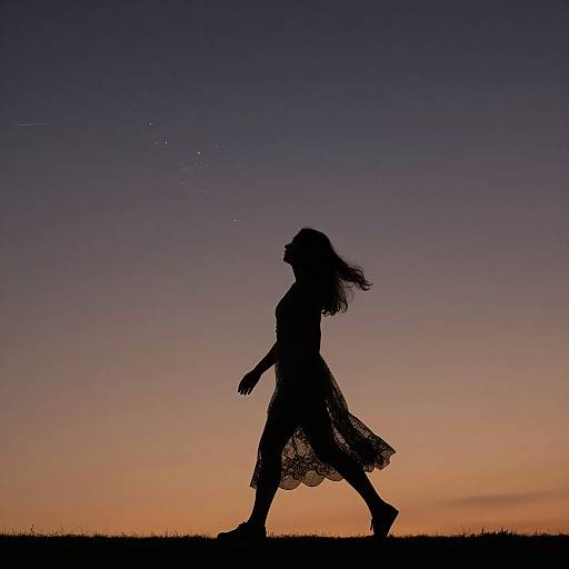 Silhouetted girl in flowing dress walks against a twilight sky with gradient colors from orange to deep blue. Evening light.