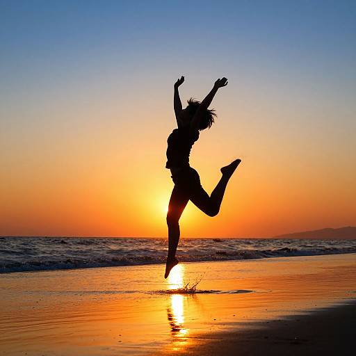 Silhouetted woman jumping against vibrant sunset on beach, with golden-orange sky and reflective ocean waves. Photograph captures dynamic motion.