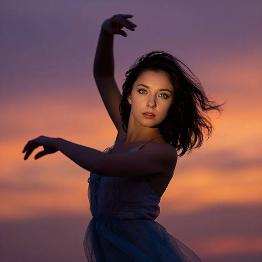 Photograph of a dark-haired woman with fair skin, wearing a black dress, striking an elegant pose against a vibrant sunset sky with purple and orange hues