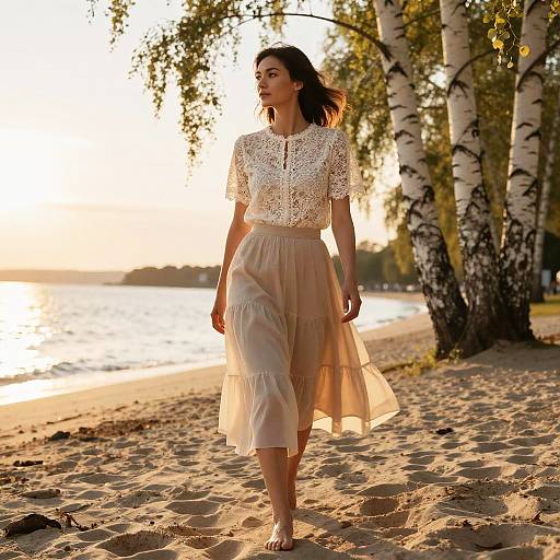 Photograph of a woman with light brown hair, wearing a lace white top and sheer, ruffled beige skirt, walking on a sunlit sandy beach