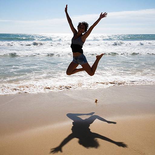 Photograph of a silhouetted woman jumping on a sunny beach, arms raised, wearing a striped tank top and shorts, with her shadow on