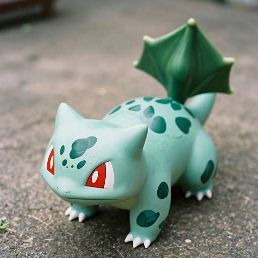 Photograph of a green, spotted, bipedal Pokémon with red eyes, small white claws, and a dark green leaf-like tail, standing on