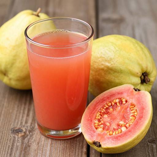 Photograph of a glass of vibrant red papaya juice, beside whole papayas and a halved papaya revealing orange seeds, on a rustic wooden