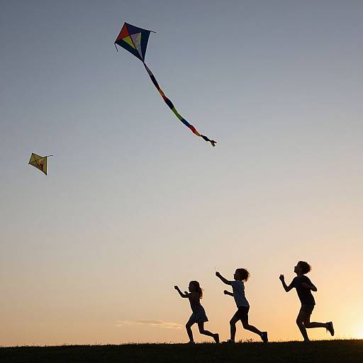 Silhouetted children running joyfully on a hill, flying colorful kites against a gradient sunset sky. Photograph, vibrant colors, playful scene.