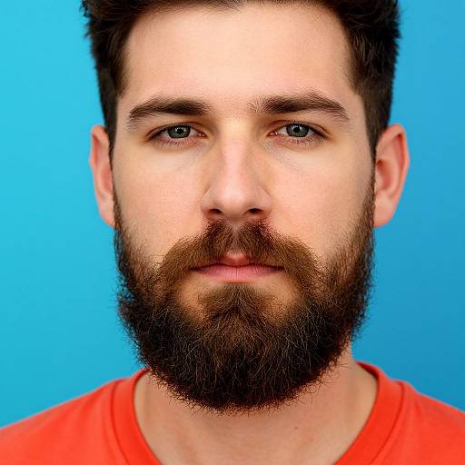 Photograph of a bearded man with blue eyes, short brown hair, wearing a red shirt, against a bright blue background.