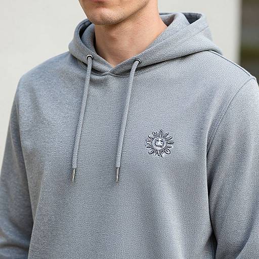 Photograph of a young man's chest and neck wearing a light gray hooded sweatshirt with a small, black sun emblem.