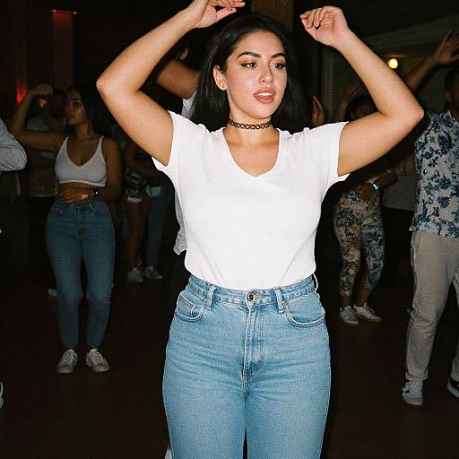 Photograph of a young woman with medium skin tone, black hair, wearing a white t-shirt, blue jeans, black choker, and adjusting her