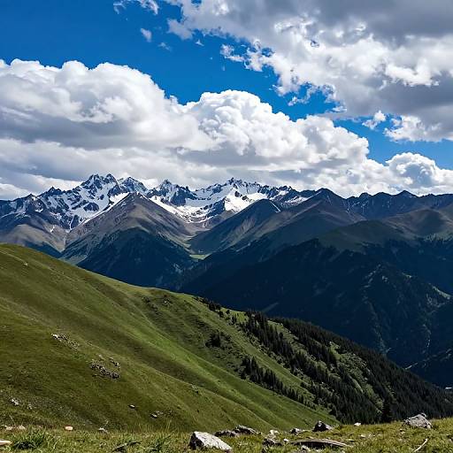 Photograph of a vibrant mountain landscape with green rolling hills, snow-capped peaks, and a bright blue sky with fluffy white clouds.