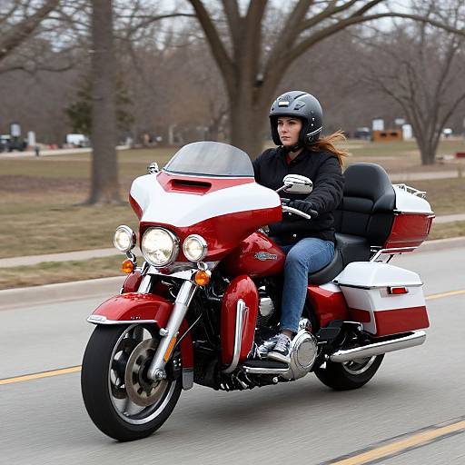 Photograph of a woman with light brown hair in a black helmet, black jacket, and blue jeans, riding a red and white Harley-Davidson