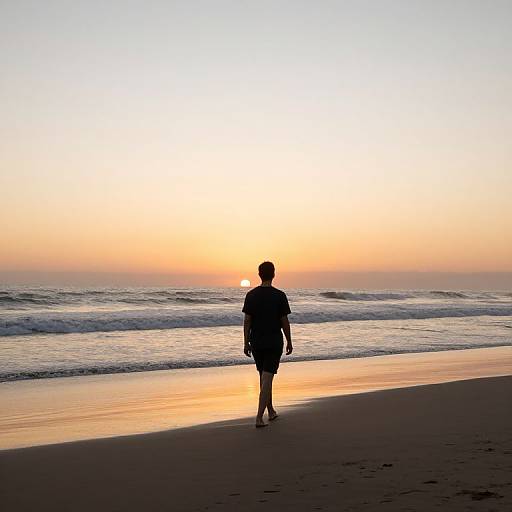 Photograph of a silhouetted person walking on a beach at sunset, with the sun low on the horizon, casting golden light on the water