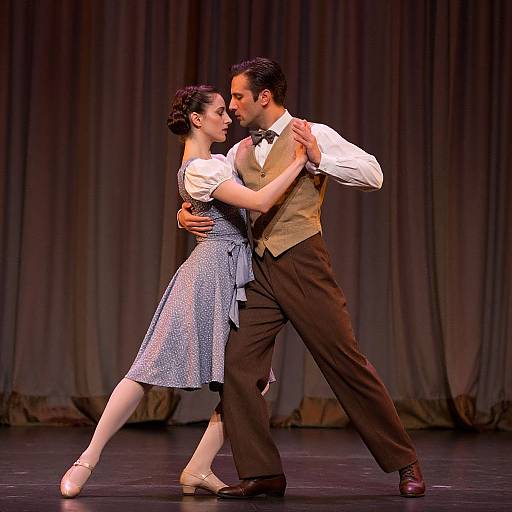 Photograph of a couple dancing waltz on stage; man in brown vest and bow tie, woman in blue polka-dot dress, against dark
