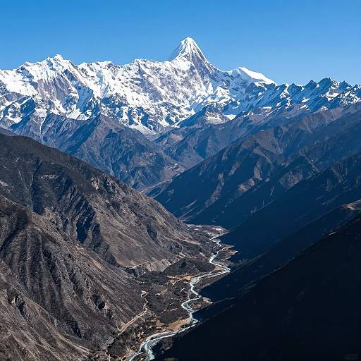 Photograph of a snowy mountain peak under a clear blue sky, with a winding river valley below and dark, rocky mountainsides.