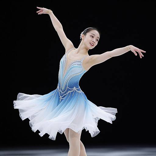 Photograph of an Asian ballerina in a blue and white, beaded, sleeveless tutu, gracefully dancing with arms extended against a black