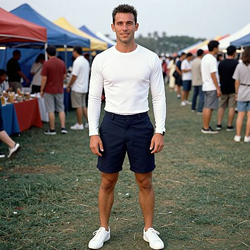 Photograph of a handsome, muscular man with short dark hair, wearing a white long-sleeve shirt, black shorts, and white sneakers, standing
