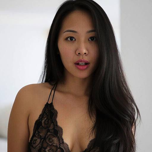 Photograph of an Asian woman with long black hair, wearing a black lace halter top, looking directly at the camera with parted lips, against a